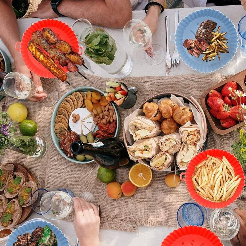 Diverse food items on a table with people around, including meats, vegetables, and drinks.
