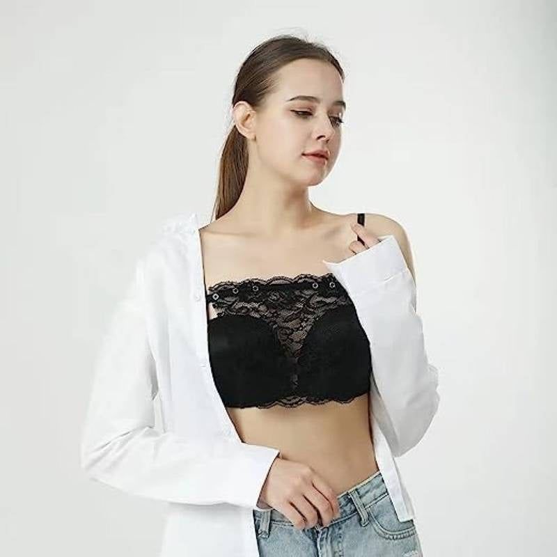 Woman wearing a black lace bralette with a white shirt and jeans on a light gray background