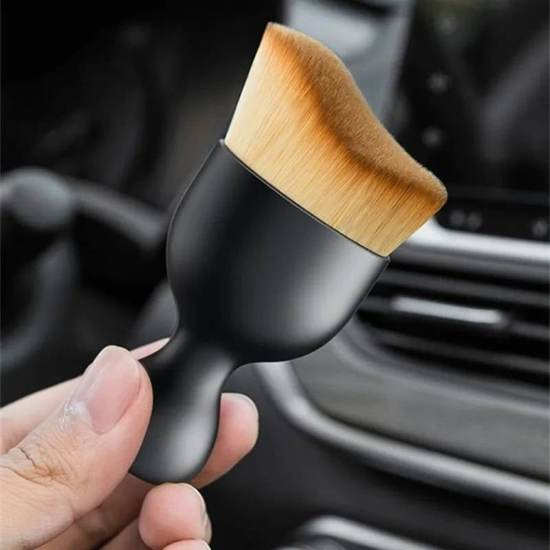 Black makeup brush with wooden tip held by a hand against a car interior background