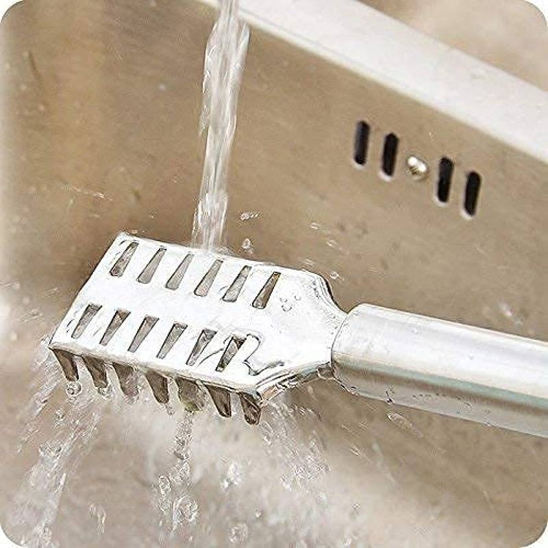 Metal bath brush being rinsed under running water in a sink.