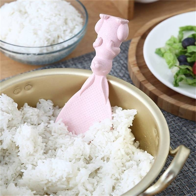 Pink owl-shaped spoon in a bowl of rice with a salad in the background
