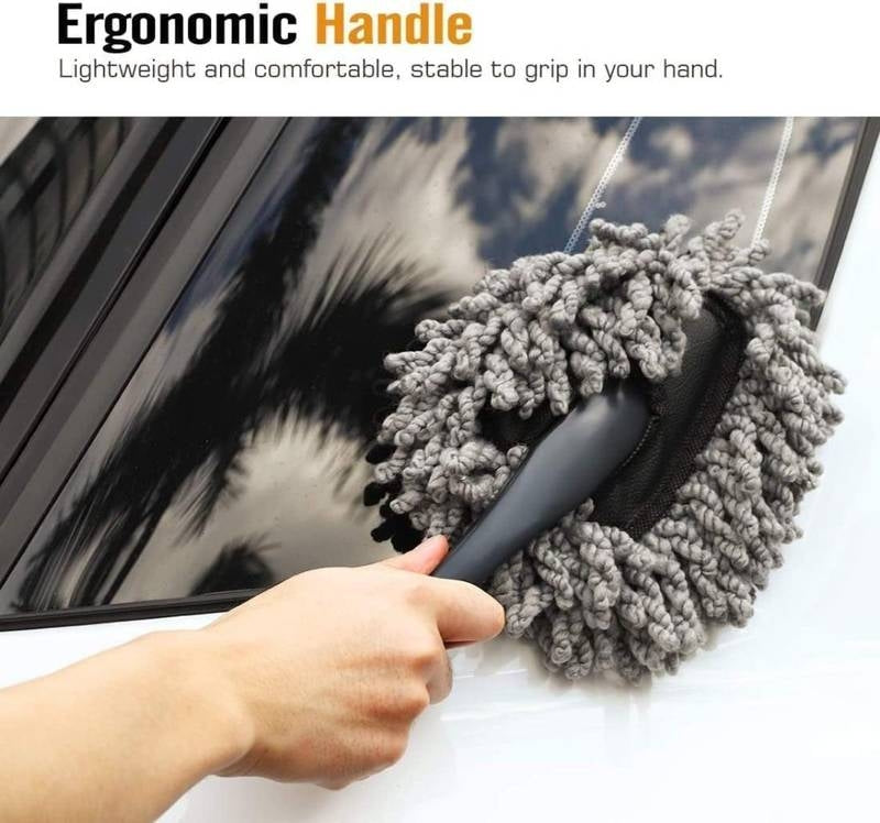 Car cleaning brush with gray bristle head and black handle being used on a car window.