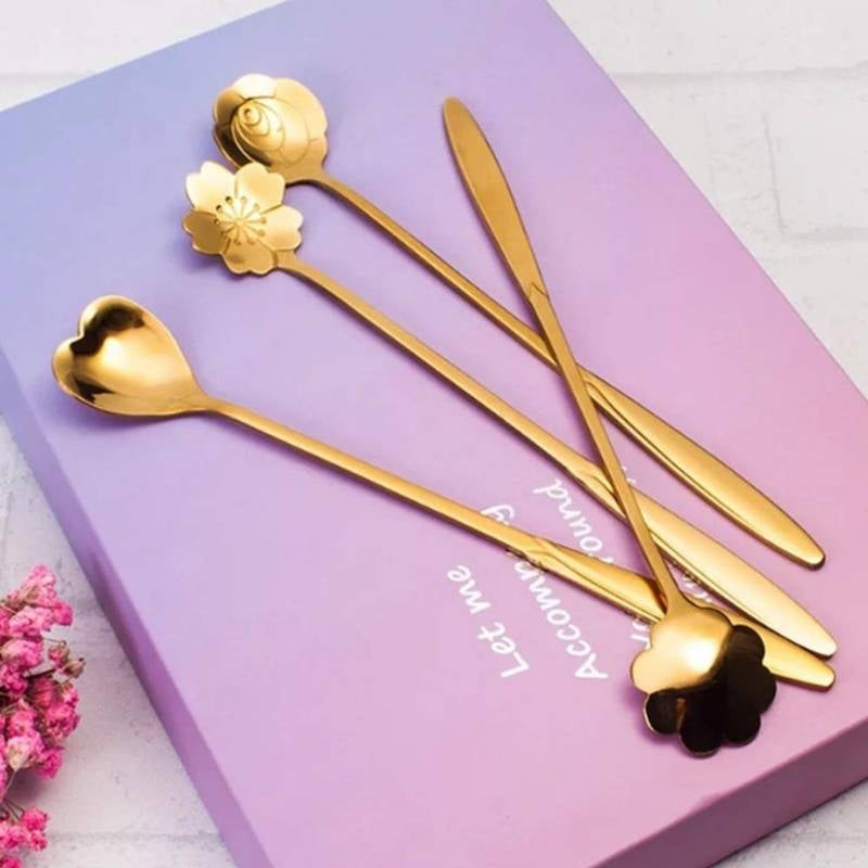 Set of gold floral spoons on a pink box with a white background