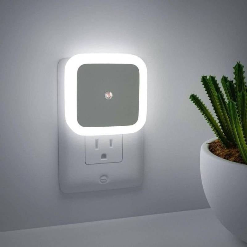 Square night light attached to a wall socket with a cactus plant in the background.
