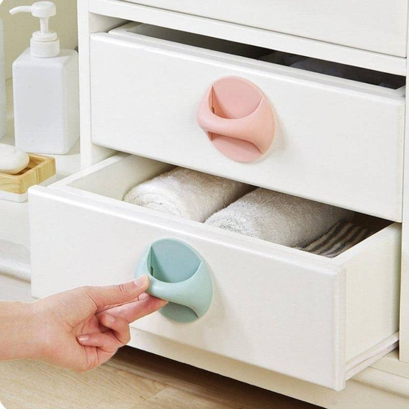 Hand opening a white drawer with pink and green drawer stoppers.