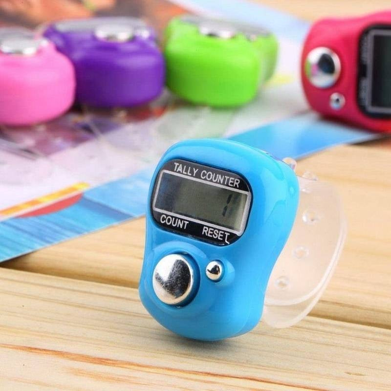 Blue digital tally counter on a wooden surface with colorful items in the background