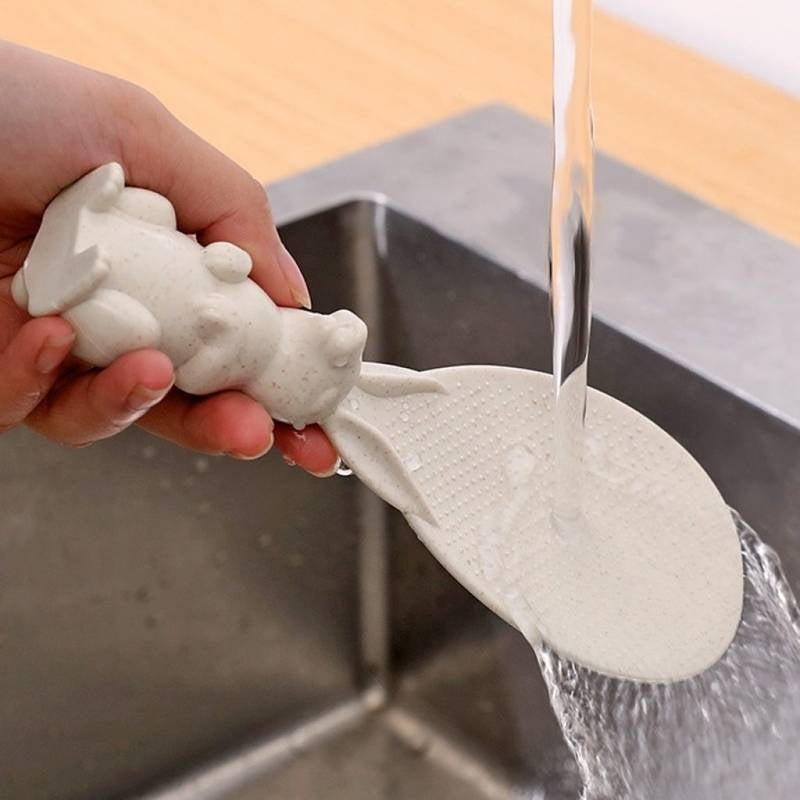Hand holding a white silicone soap saver with water flowing from it over a sink.
